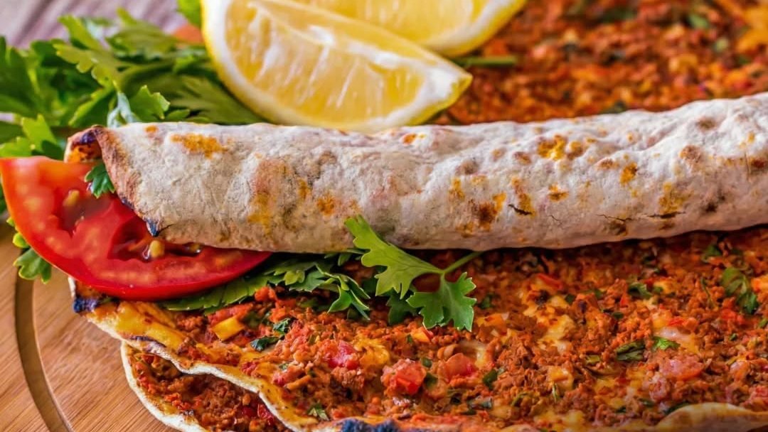 Twee lahmacun op een houten plank, met partjes citroen, tomaat, peterselie en een opgerolde exemplaar erbovenop.